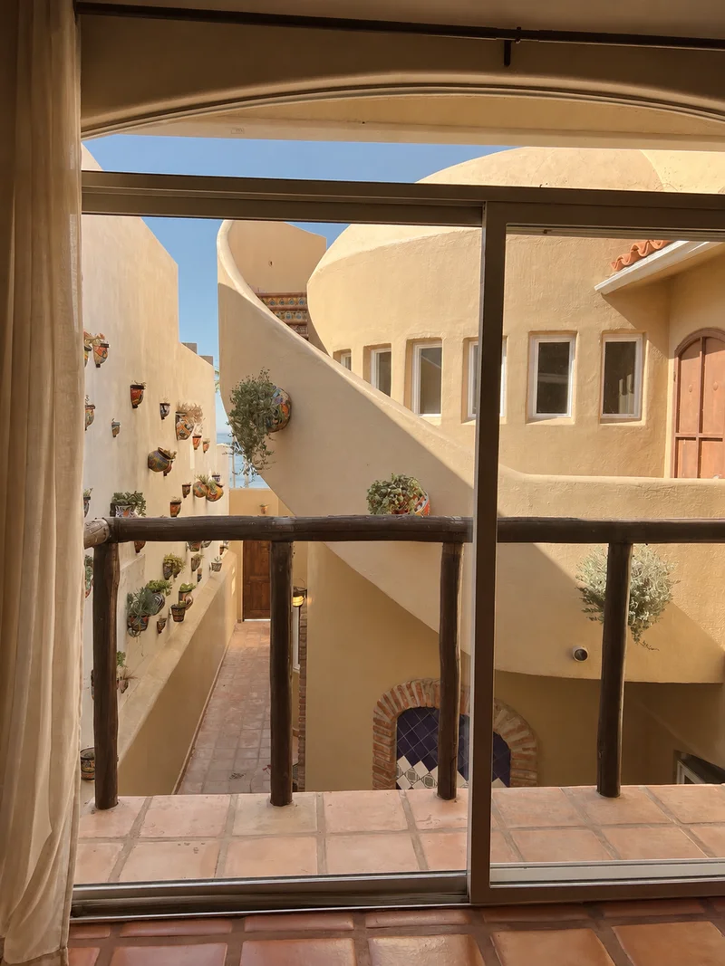The courtyard seen from inside through a sliding door: curved stucco walls, arched windows, and planted pots stepping down the wall.