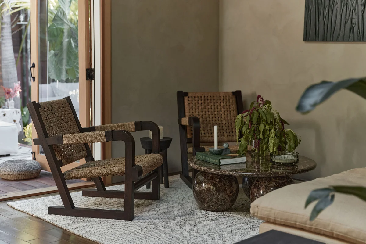 The cane armchairs and stone table from across the room, the ottoman running along the window wall.