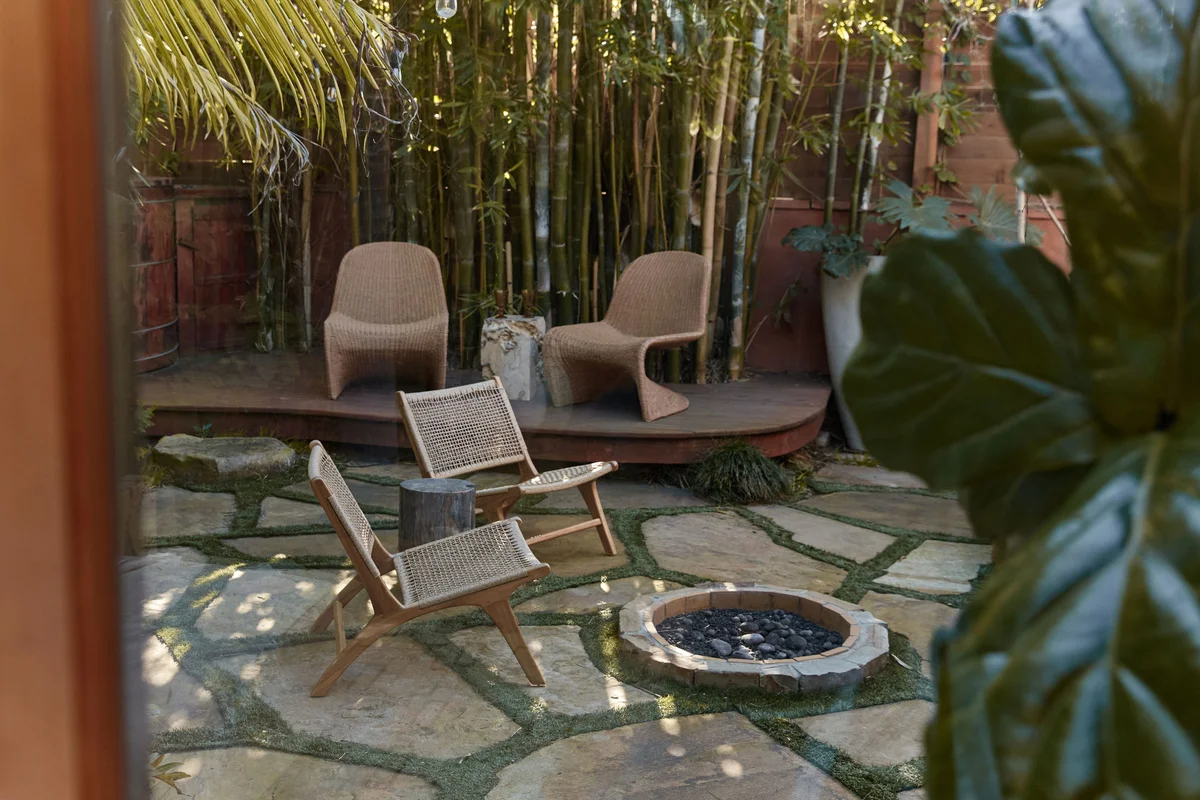 The courtyard: two curved lounge chairs and a slung timber chair set around a low fire bowl on flagstone paving, with bamboo growing close on every side.