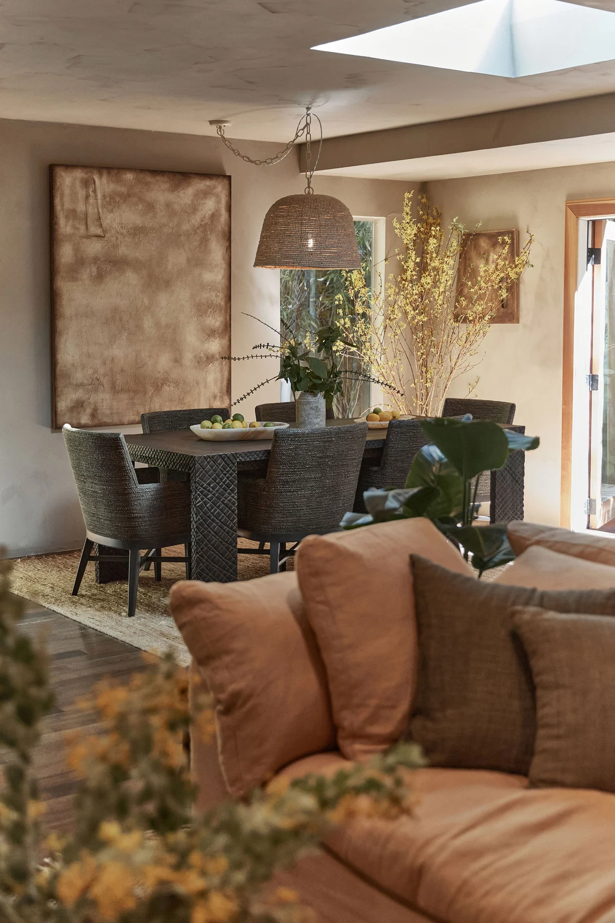 The dining room seen across the living room, rust cushions on the sofa in the foreground and daylight falling from a skylight.